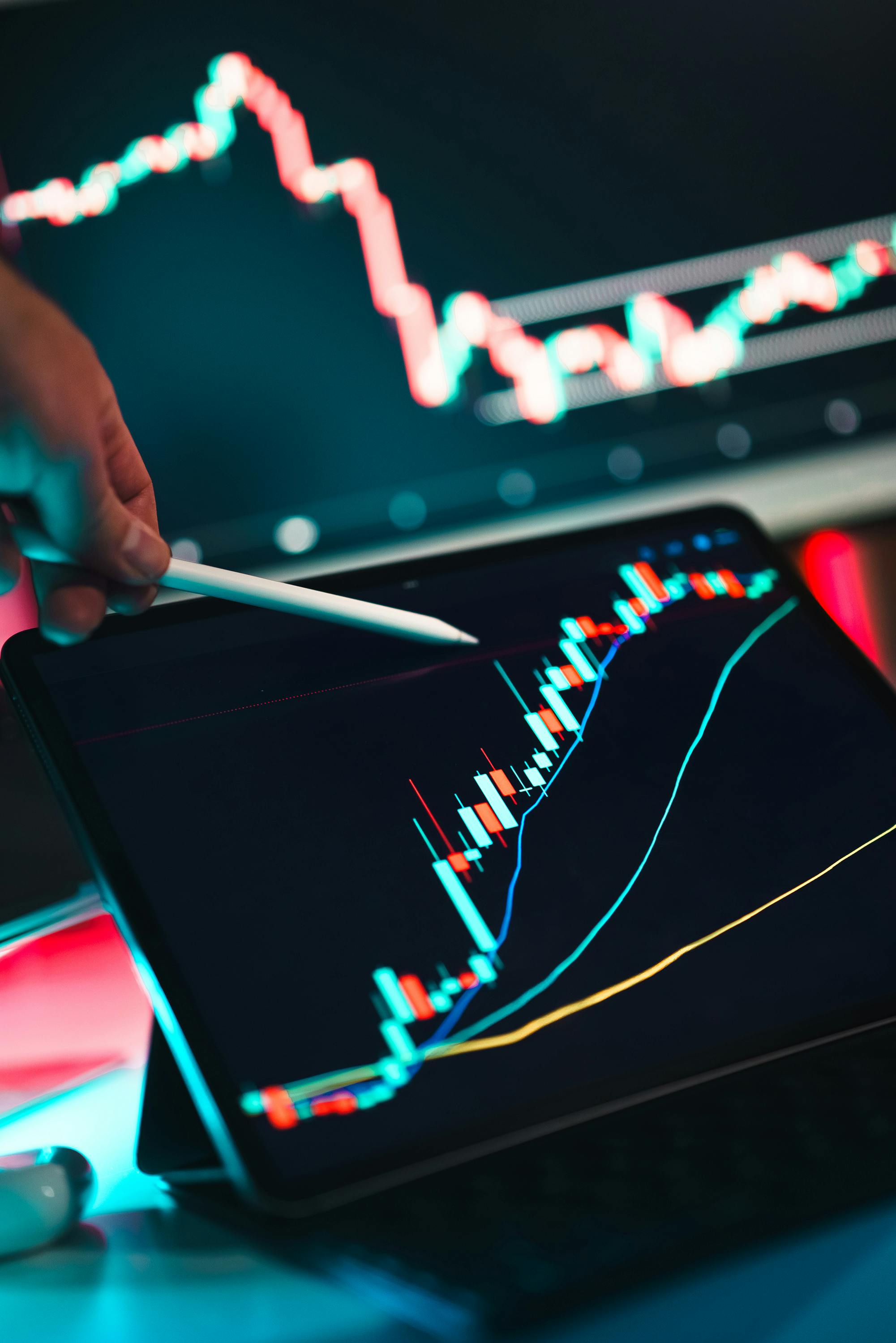 A hand holding a smartphone displaying stock market graphs and data with colorful light reflections in the background.