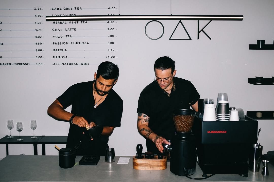Baristas preparing coffee beneath dimensional OAK wall logo signage at Oak & Saint café and wine bar.