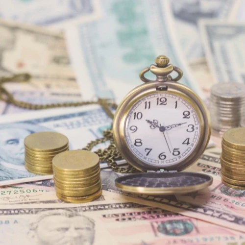 Vintage pocket watch surrounded by cash and stacks of coins, symbolizing time is money concept and financial planning.