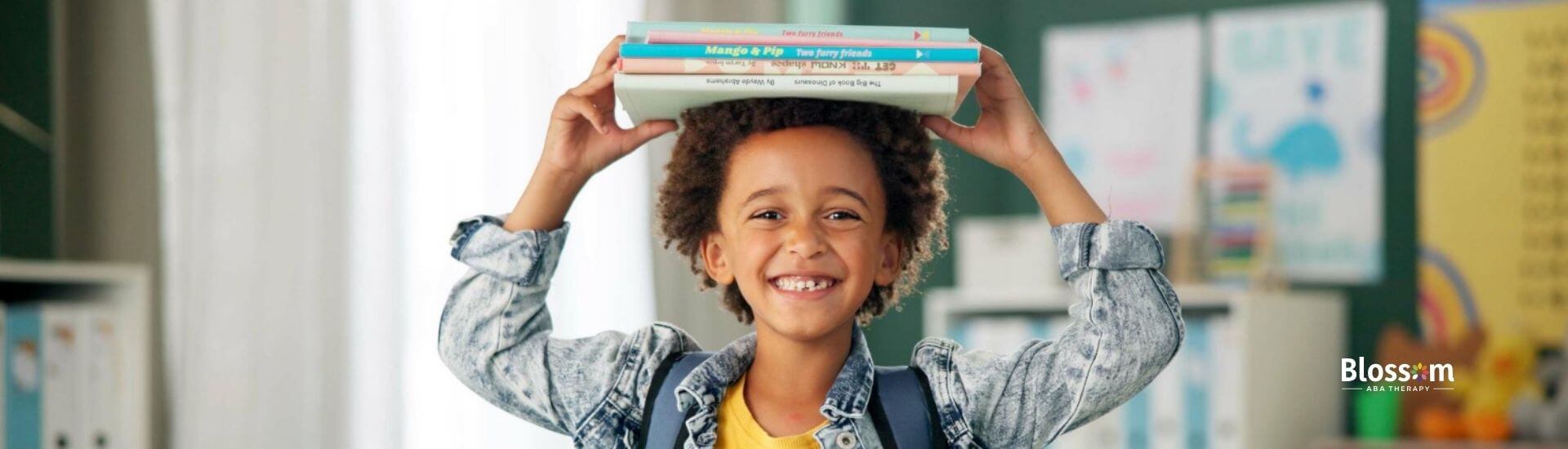 Smiling child with books on head in classroom.