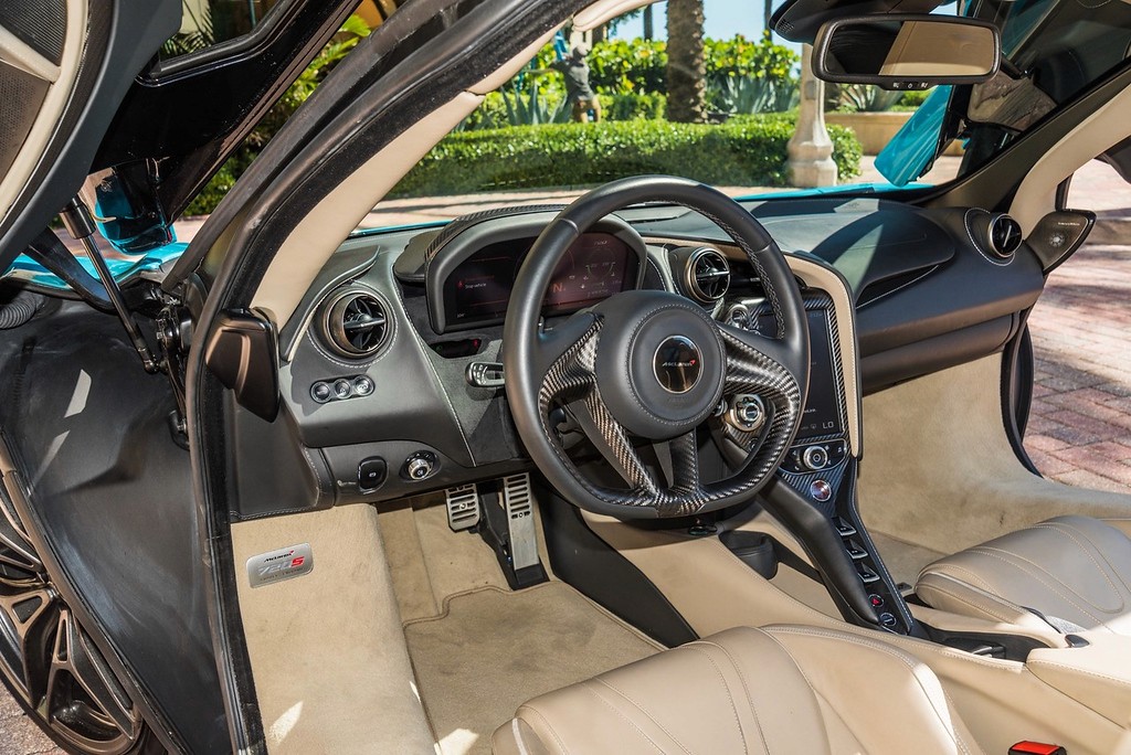 A stunning blue McLaren 720S with dihedral doors open, parked in a luxurious setting with palm trees and an elegant building in the background. This exotic supercar features a sleek design, powerful twin-turbo V8 engine, and unparalleled performance, making it the perfect choice for a luxury car rental experience.