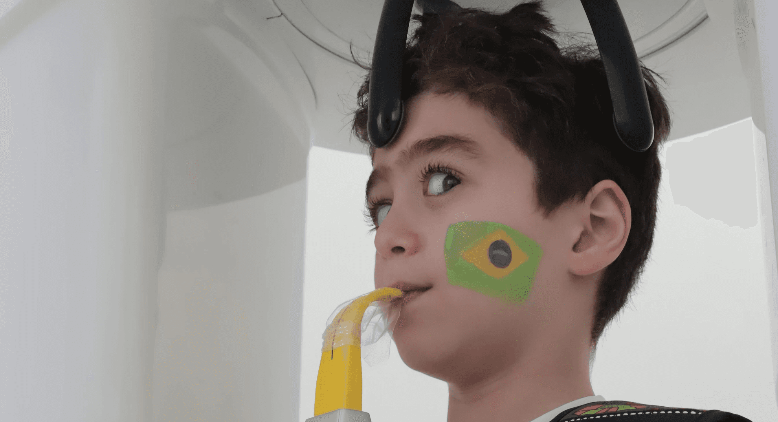 A kid undergoing a teeth checkup using a panoramic dental X-ray machine to examine baby teeth, by Invisalign Center