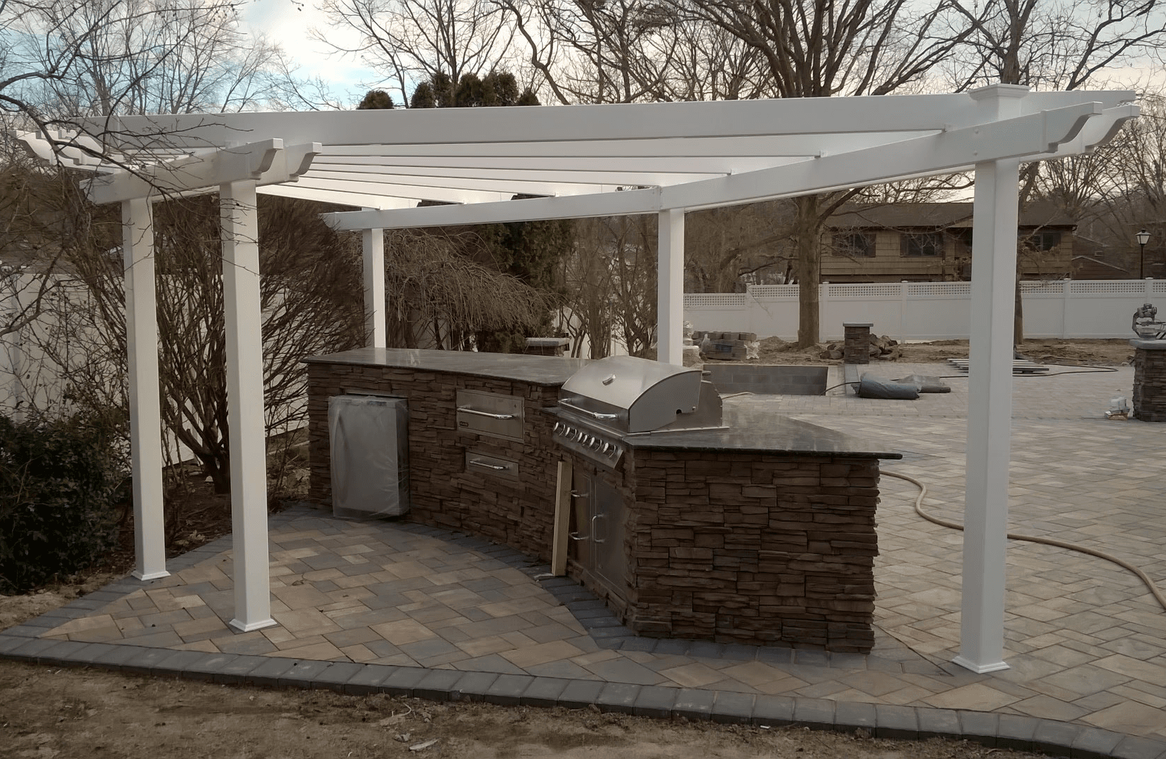Outdoor kitchen with white pergola and brown stacked-stone base