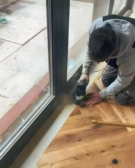 Bodenleger schneidet Parkett präzise am Fensterbereich zu