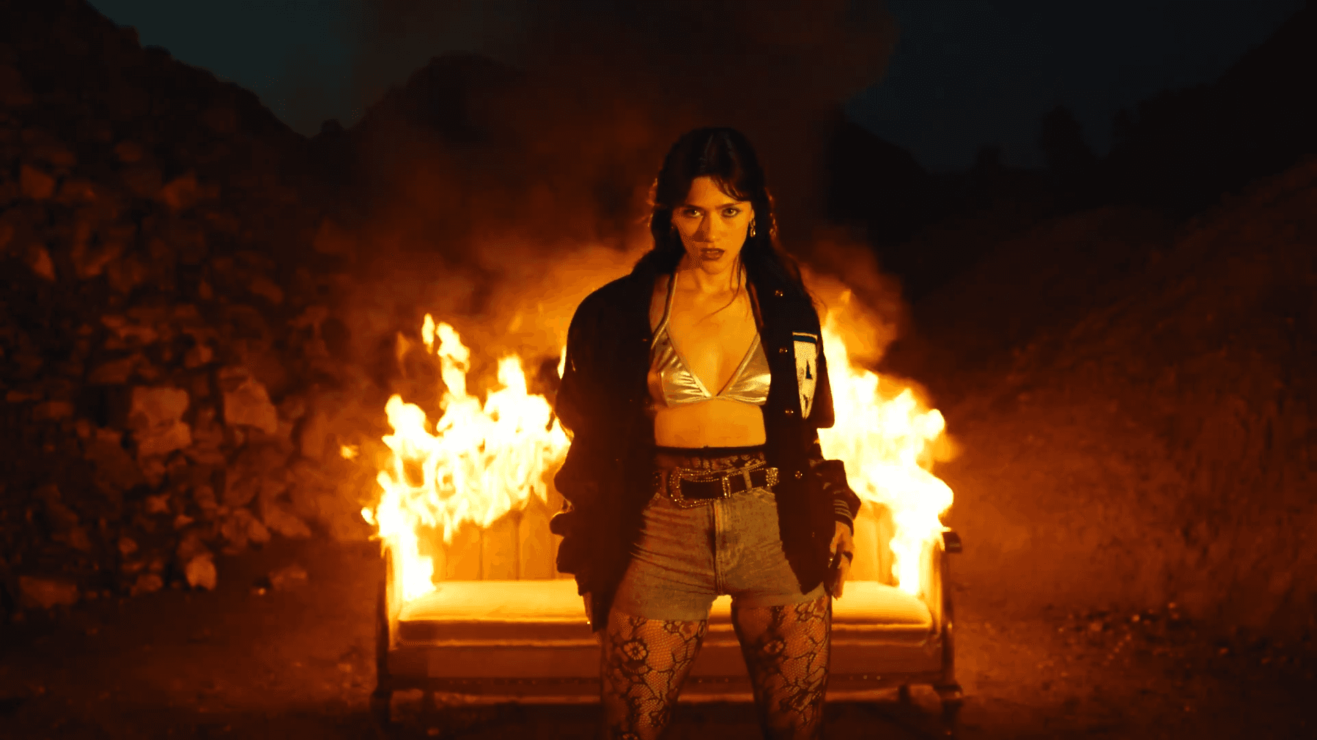 woman standing infront of brunging sofa couch at night time scary loking into camera fire