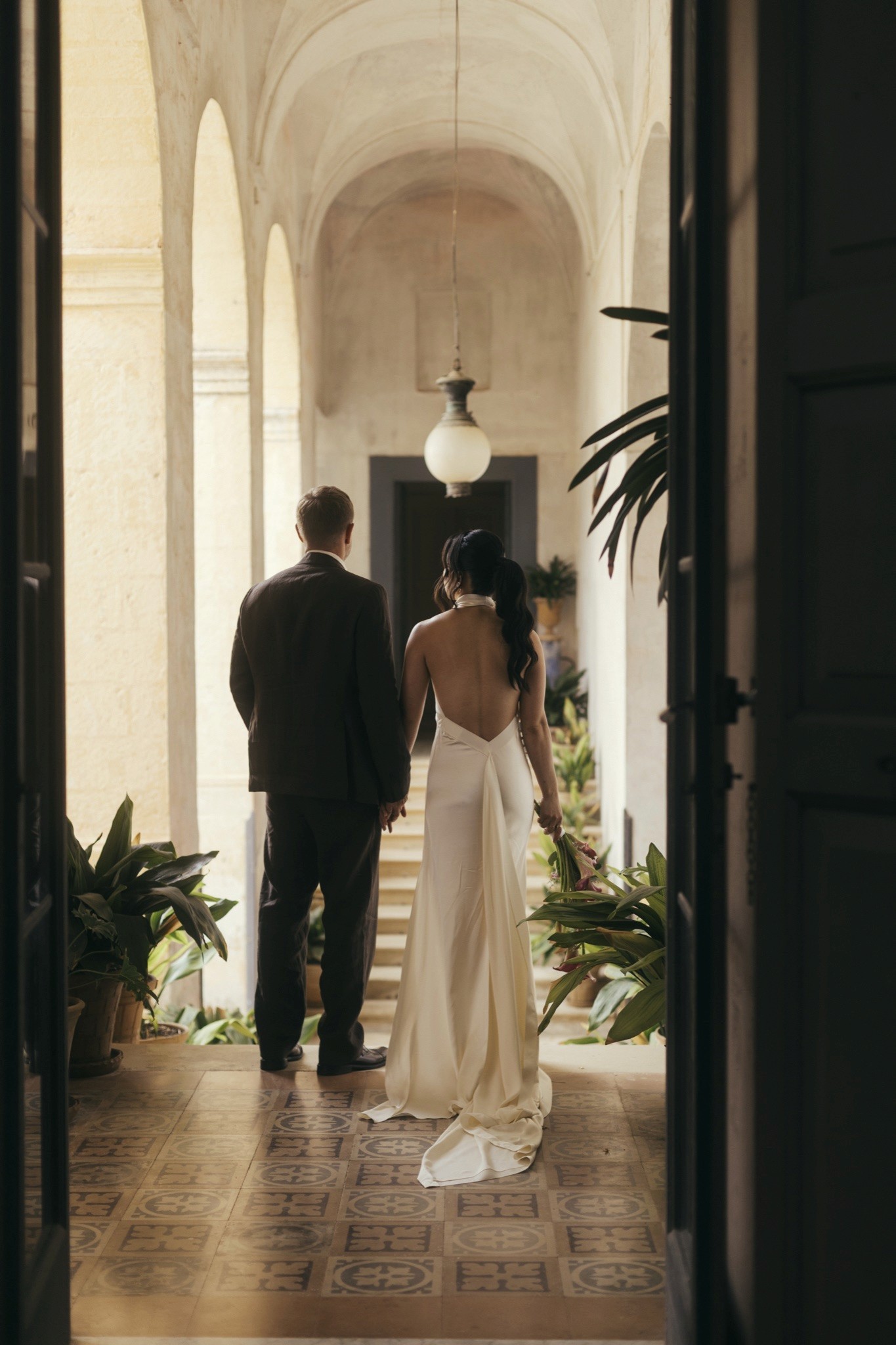 Toey and Otto standing together in an arched cloister, seen from behind