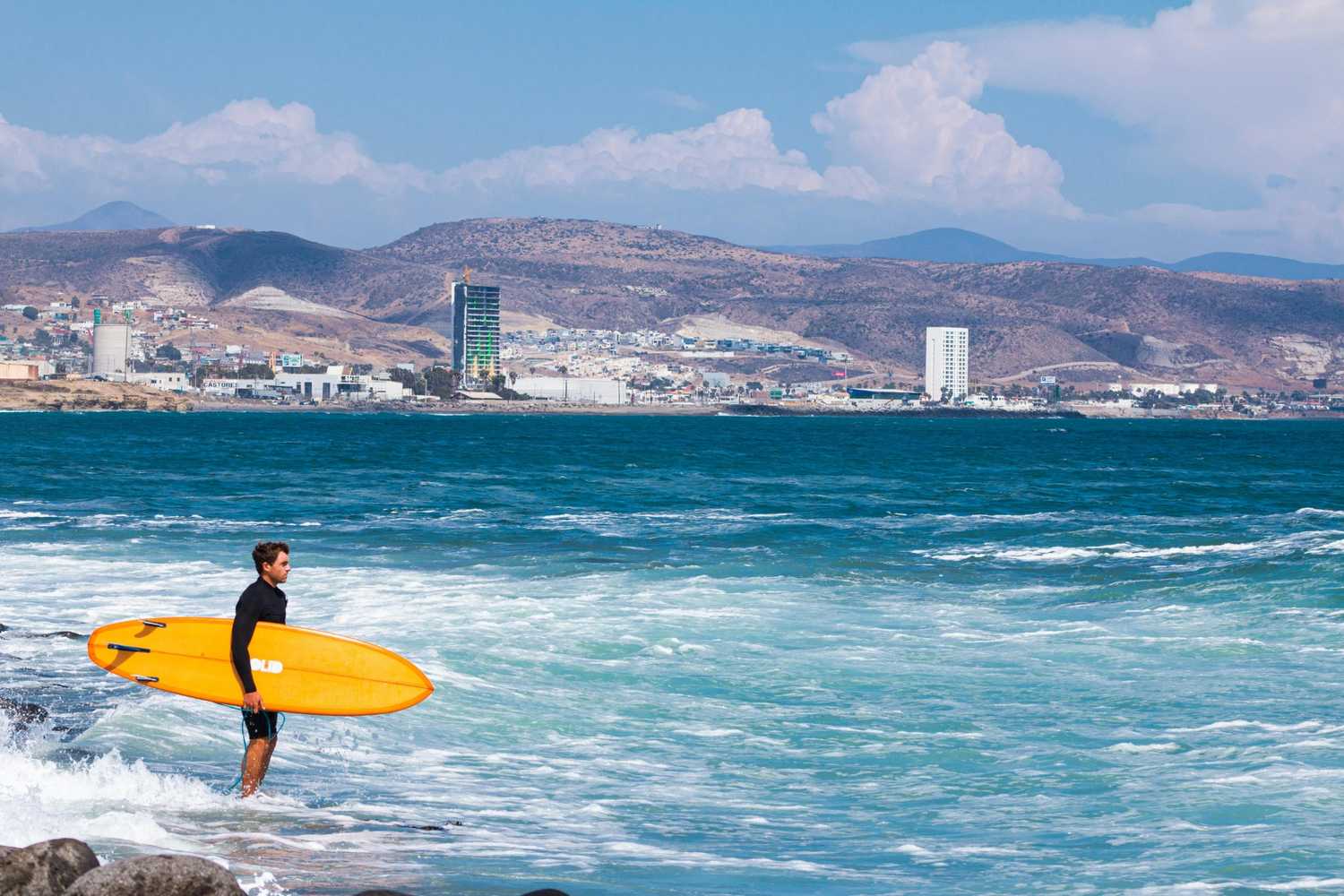Surfer sitting on a board watching the sunset over a coastal city — surfboard rental in Mexico