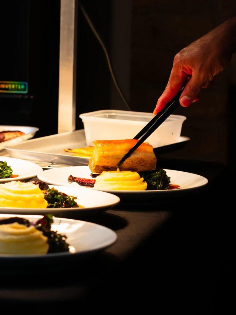 Plating pork belly with tongs on the pass