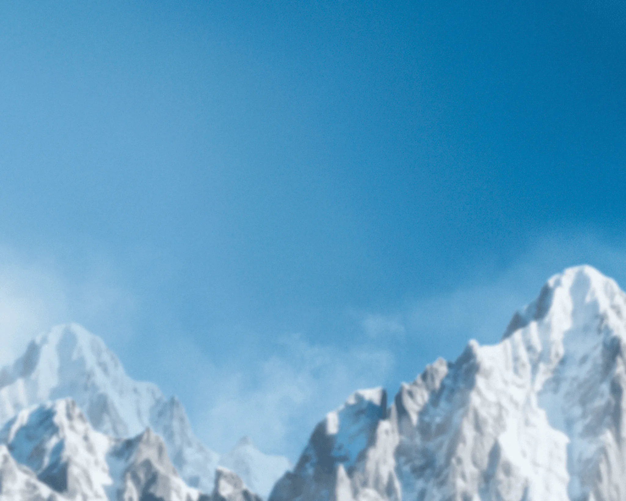 Snow-capped mountains under a clear blue sky, with a hint of clouds in the background