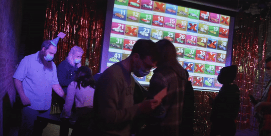 Animated image showing people arriving at the show. There is a projection screen showing many toy cars in the background.