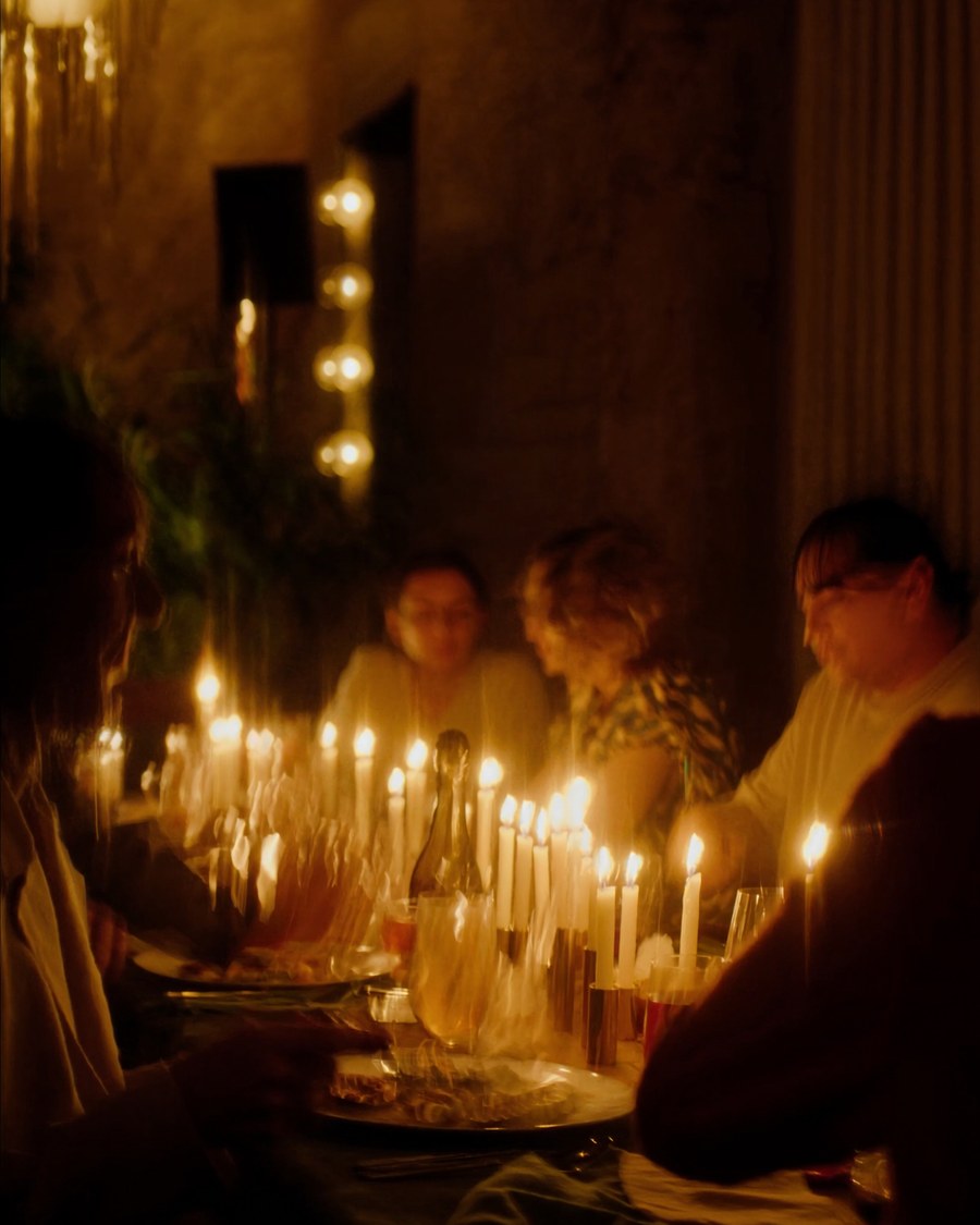 A long candlelit table of friends at dinner