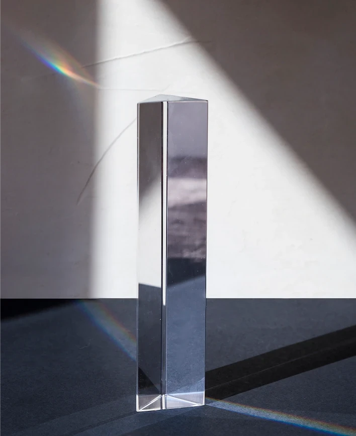 Transparent prism dispersing light into a colorful spectrum on dark surface.