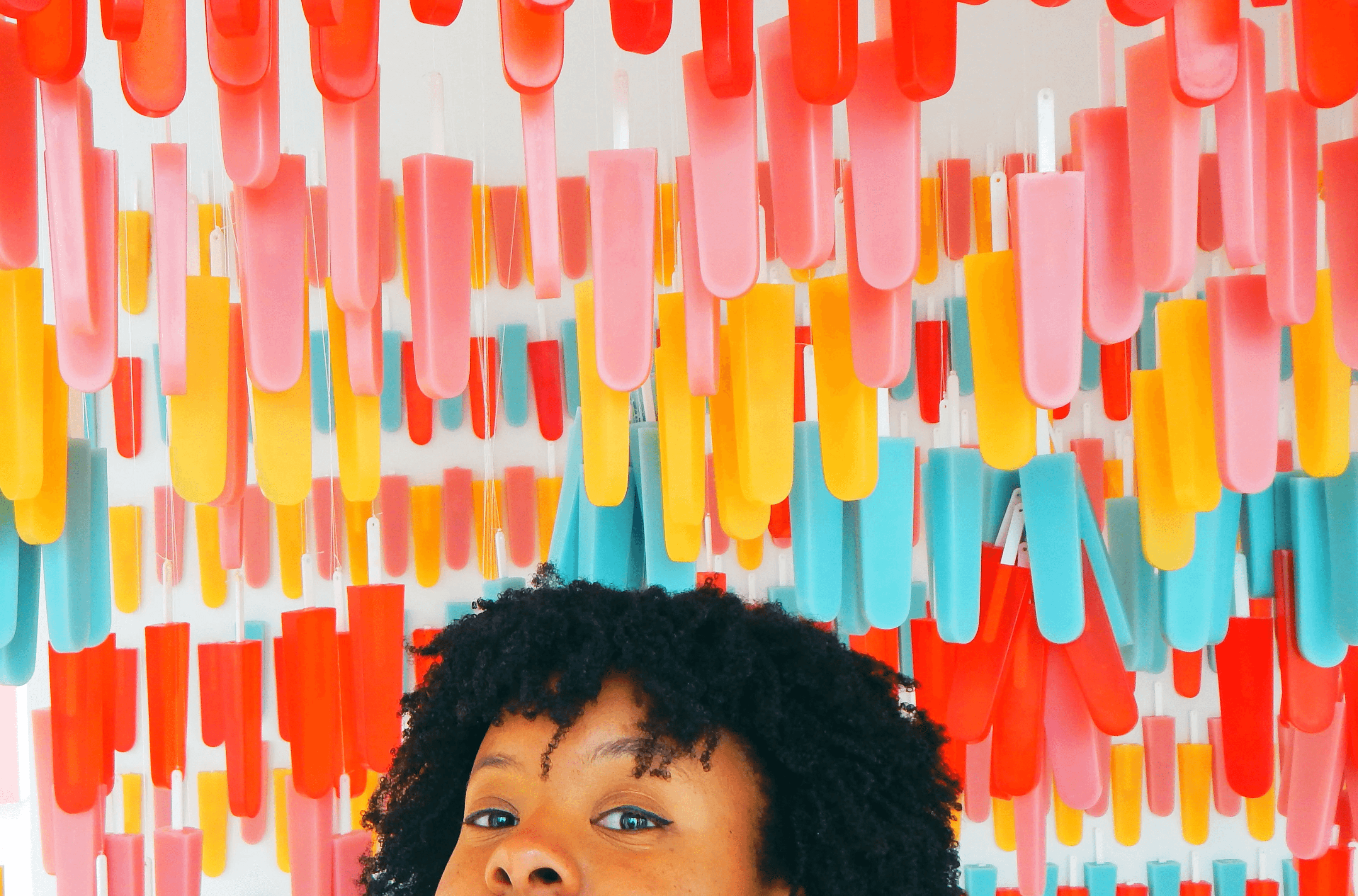 An image of Lia Zamor peaking her head up to her nose in front of a wall of hanging popsicles.