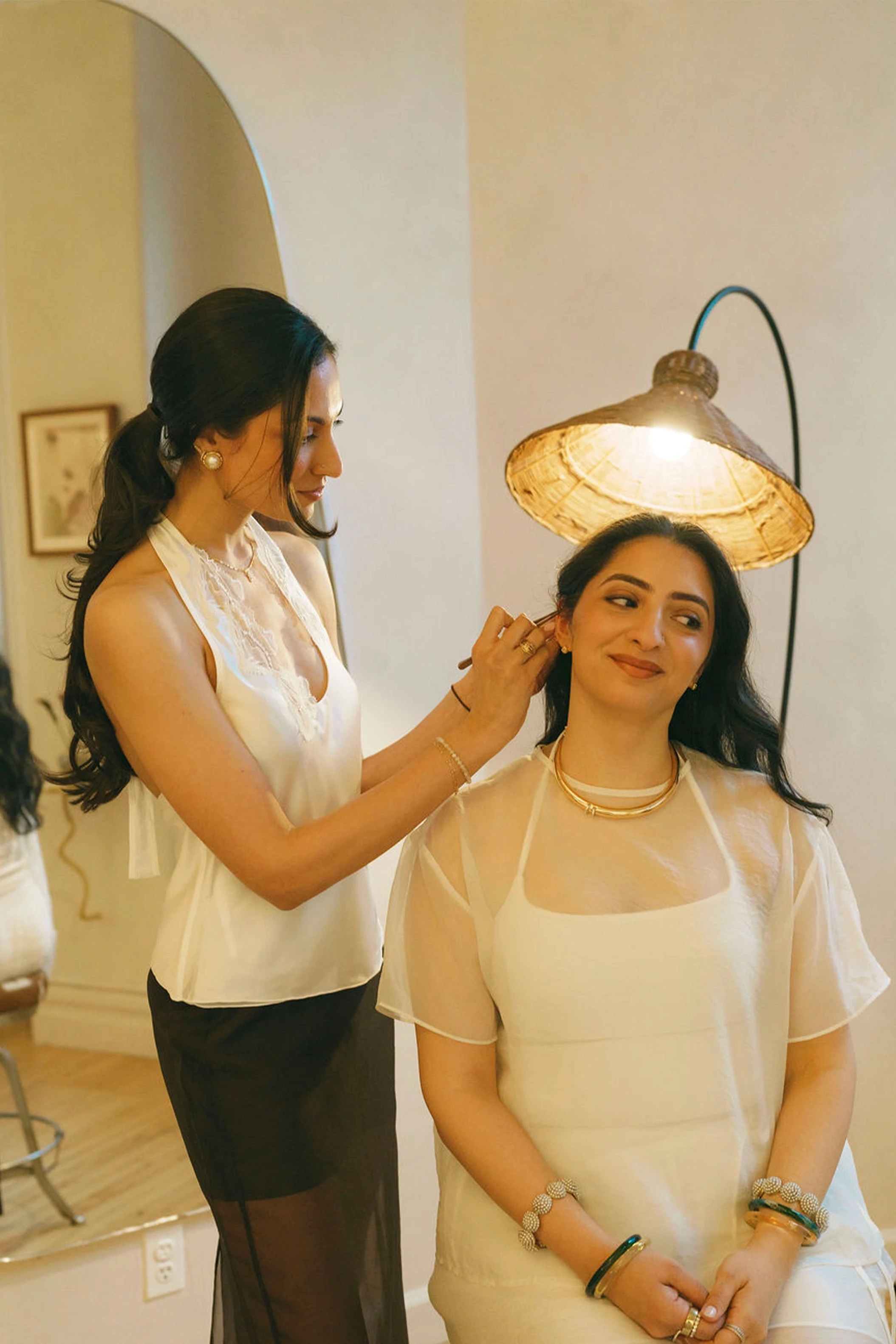 A practitioner tending to a smiling bride's ear beneath a warm pendant lamp