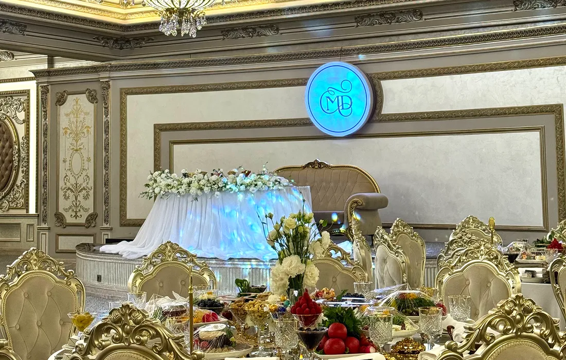 Opulent banquet hall with gold and white decor, featuring a floral-adorned platform, elegant seating, and lavish table settings.