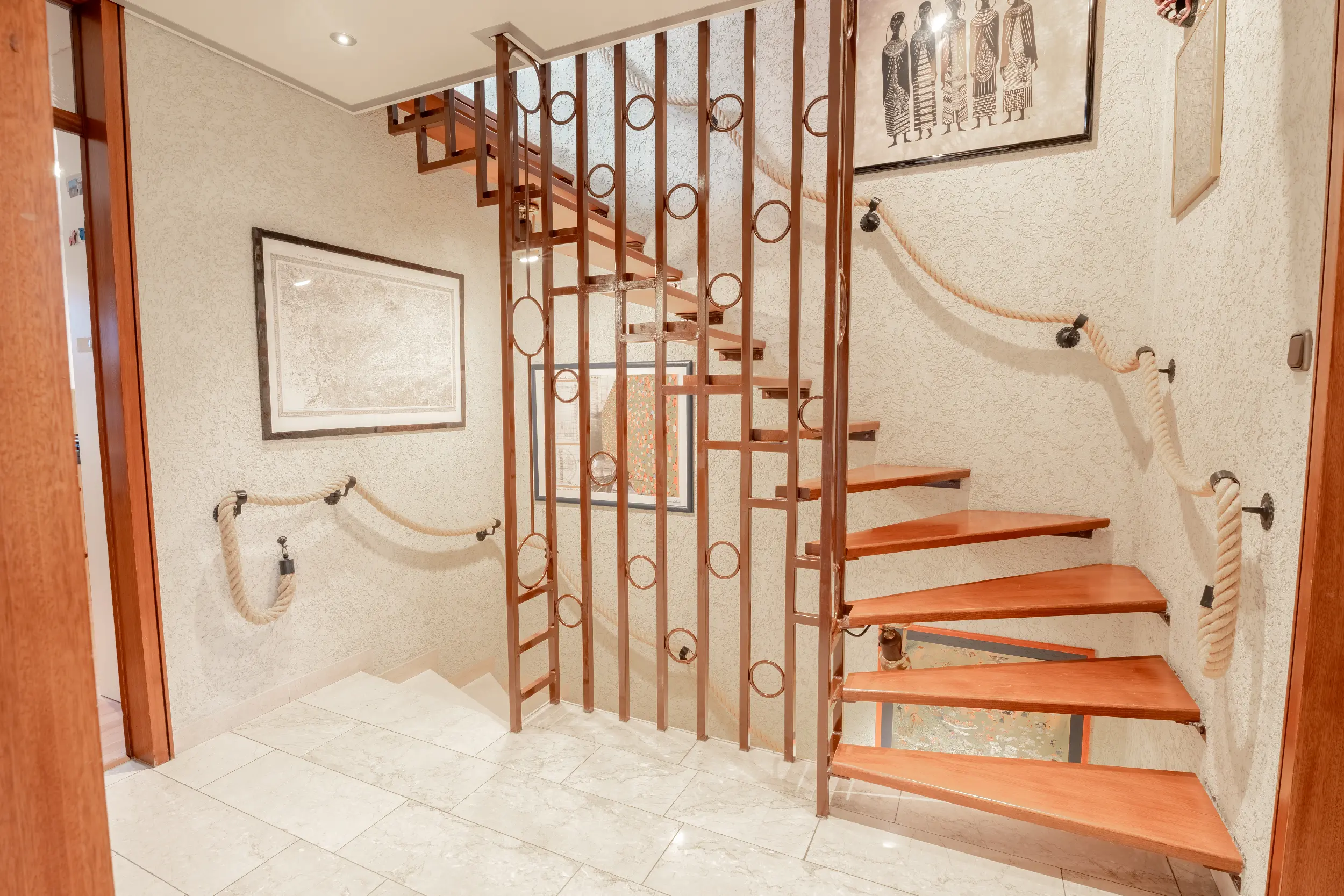 Treppenhaus im Reihenmittelhaus in Raesfeld mit offener Holztreppe, Metallgeländer, Natursteinboden und dekorativer Wandgestaltung.