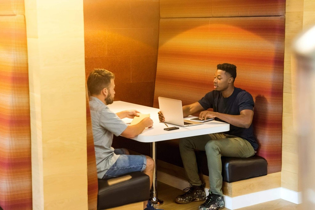 Two men having a business meeting in a cozy office booth with a laptop and notes.