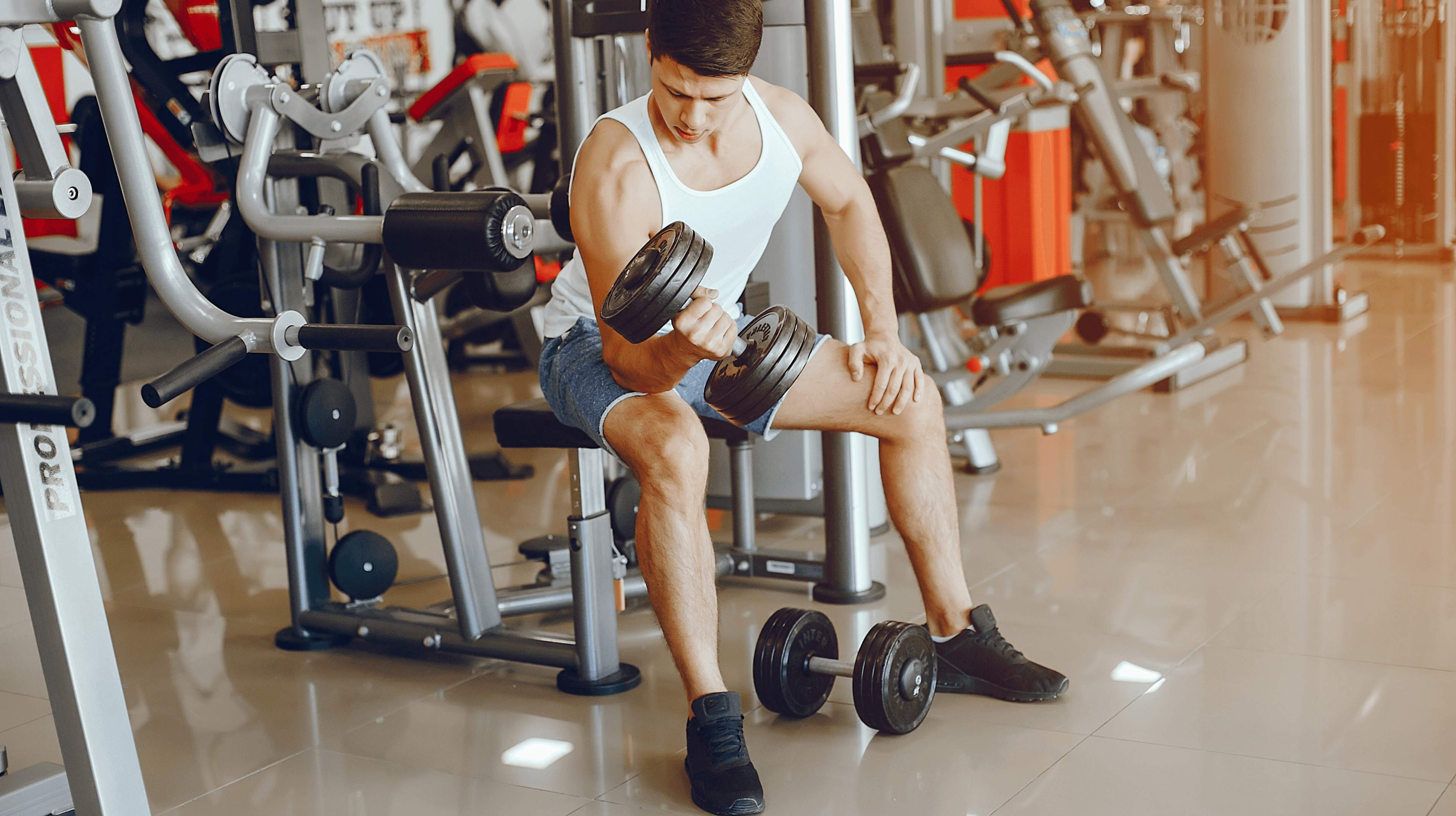 Man seated in a gym doing a dumbbell curl.