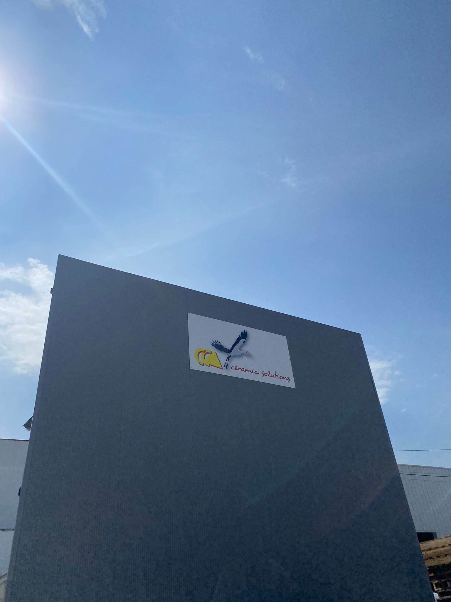 Façade extérieure d'un entrepôt avec le logo CCA Ceramic Solutions affiché sur fond de ciel bleu