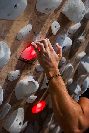 Hand greift einen leuchtenden Griff an der Shiny Wall Systemwand – präzise Grifftechnik beim Indoor-Bouldern im The Boulder Room München.