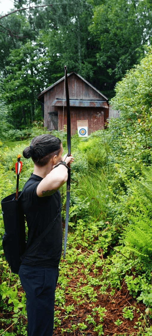 Person practicing archery in a forest, aiming toward a distant target — symbolizing focus and clarity.