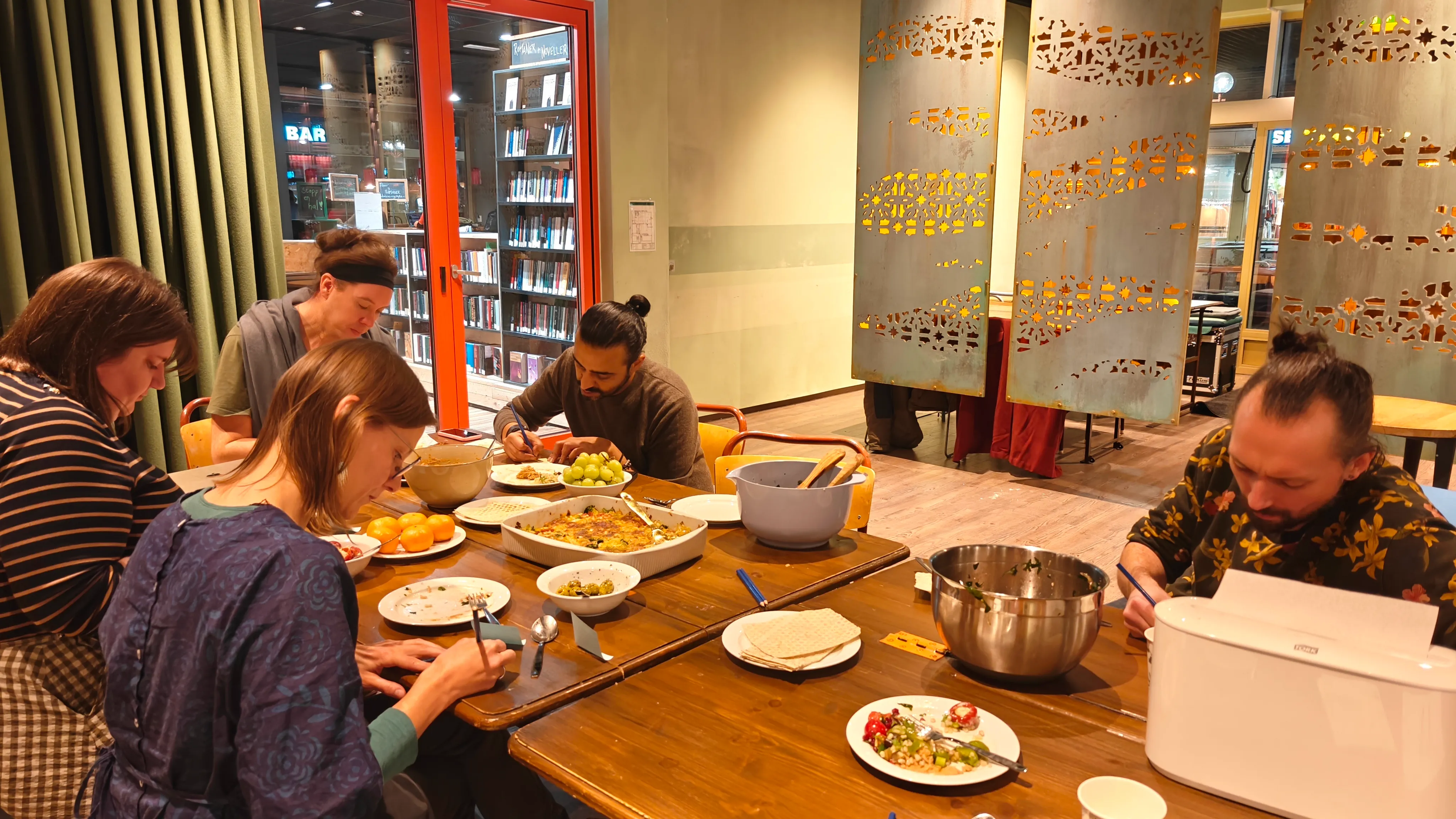 People sitting down around a table with food, writing down somethng