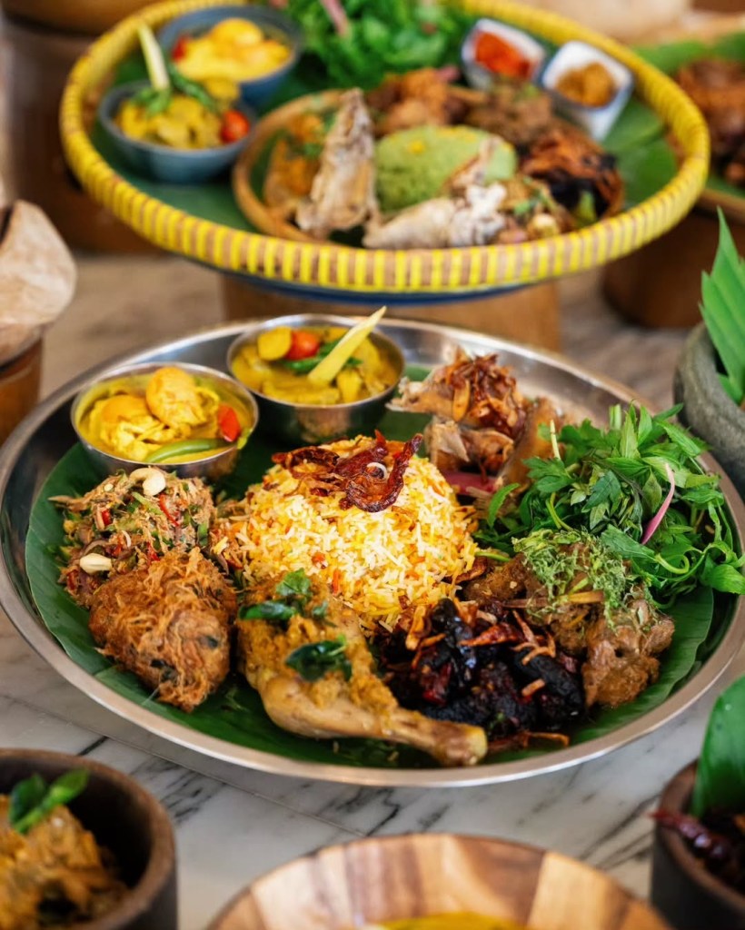 A beautifully arranged platter of traditional Malaysian dishes, featuring aromatic rice, garnished meats, vegetables, and colorful side dishes presented on a banana leaf.