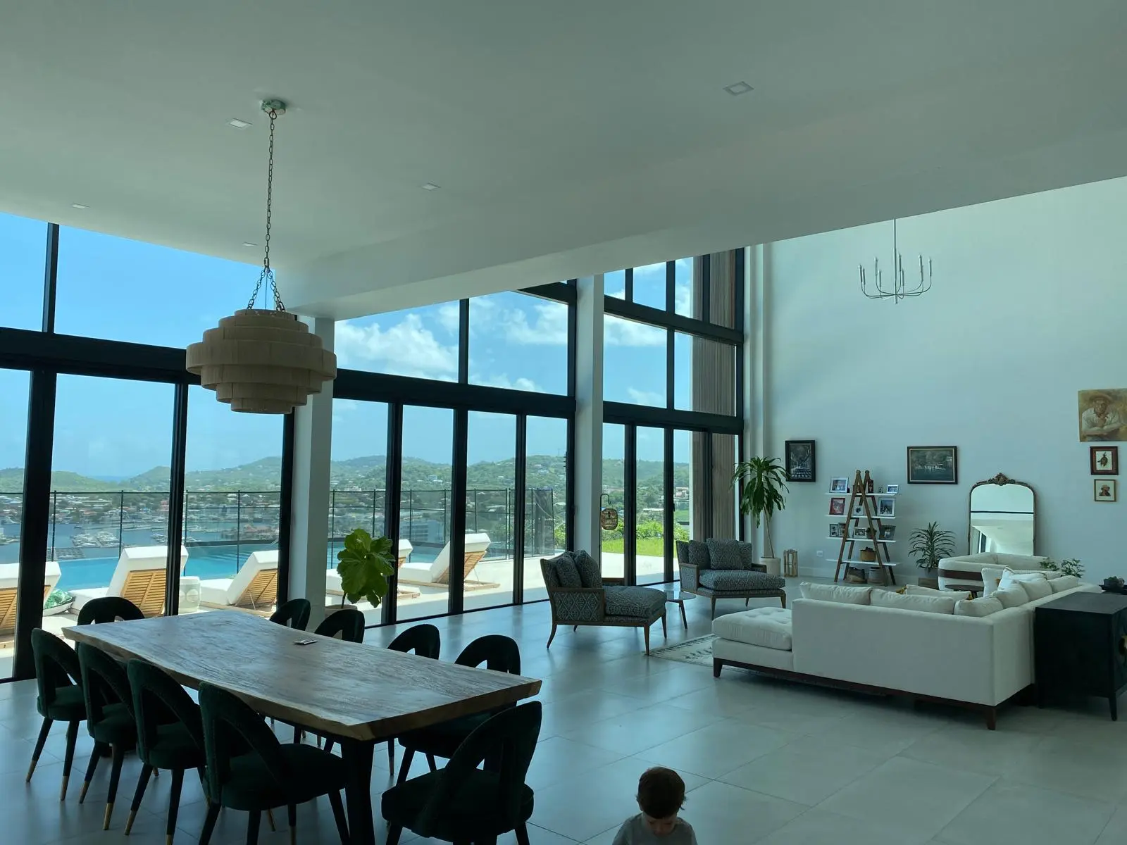 Open-plan interior of The Hill Residence in St. Lucia by Atelier International, with a live-edge dining table, seating area, and full-height windows opening to the pool terrace.