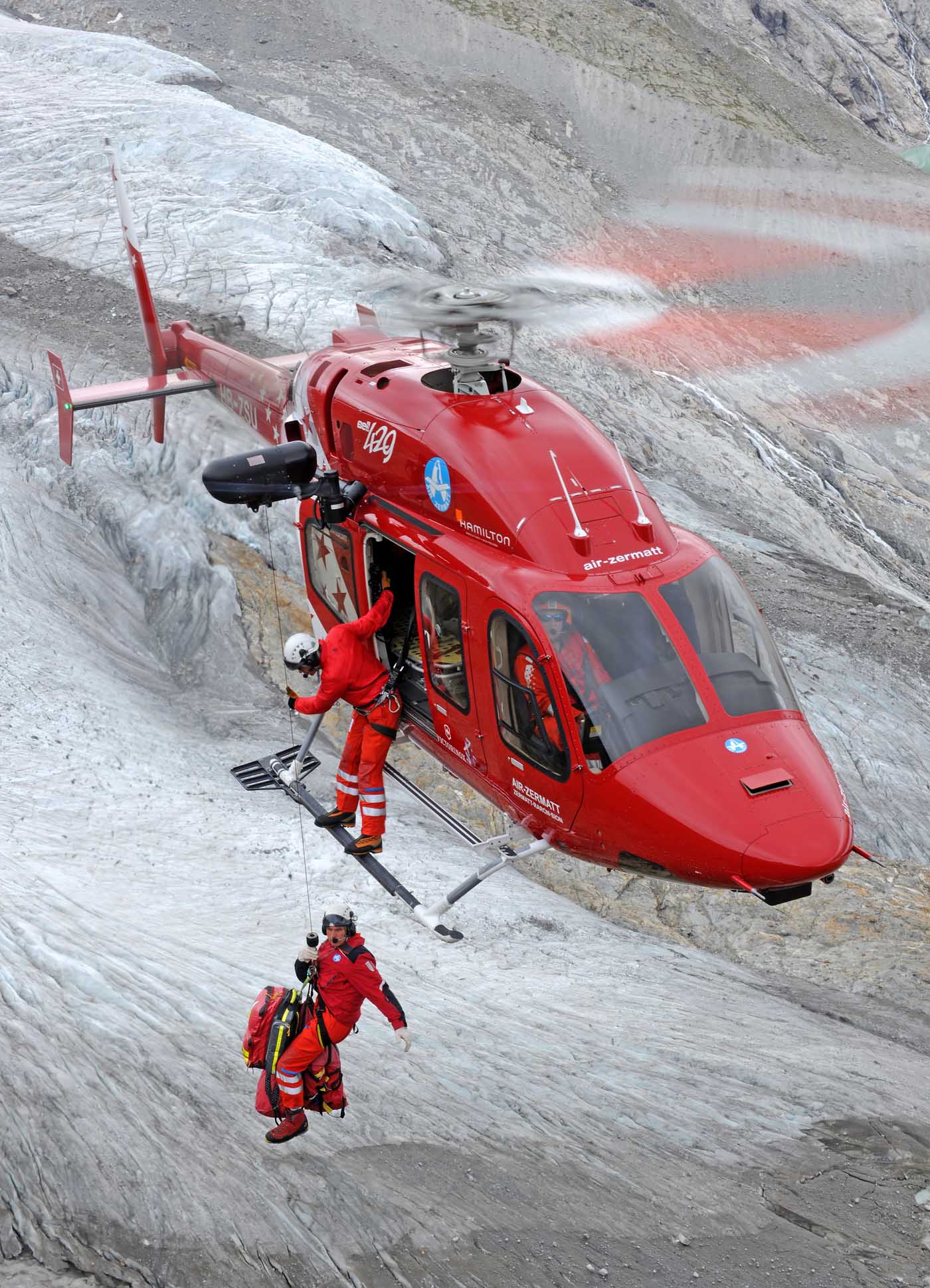 A man in orange shirt seated on a chair among trees.