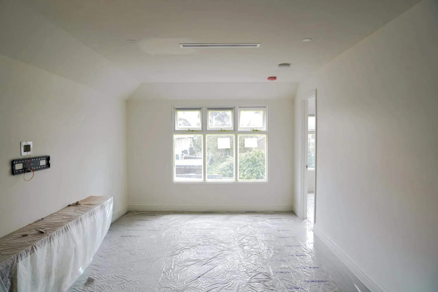 Empty room with white walls, large window, and plastic-covered floor.