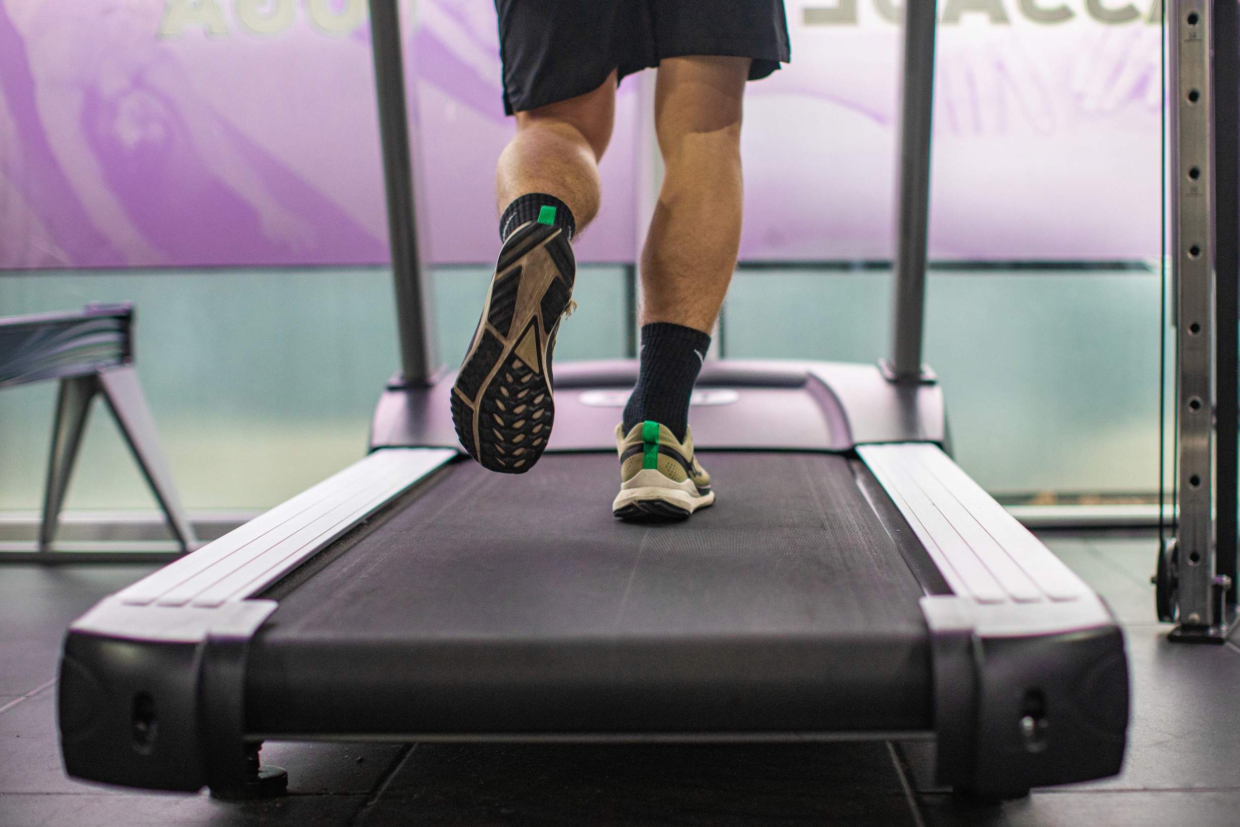 A person running on a treadmill indoors, wearing black shorts and sports shoes. The focus is on their legs, conveying motion and energy.