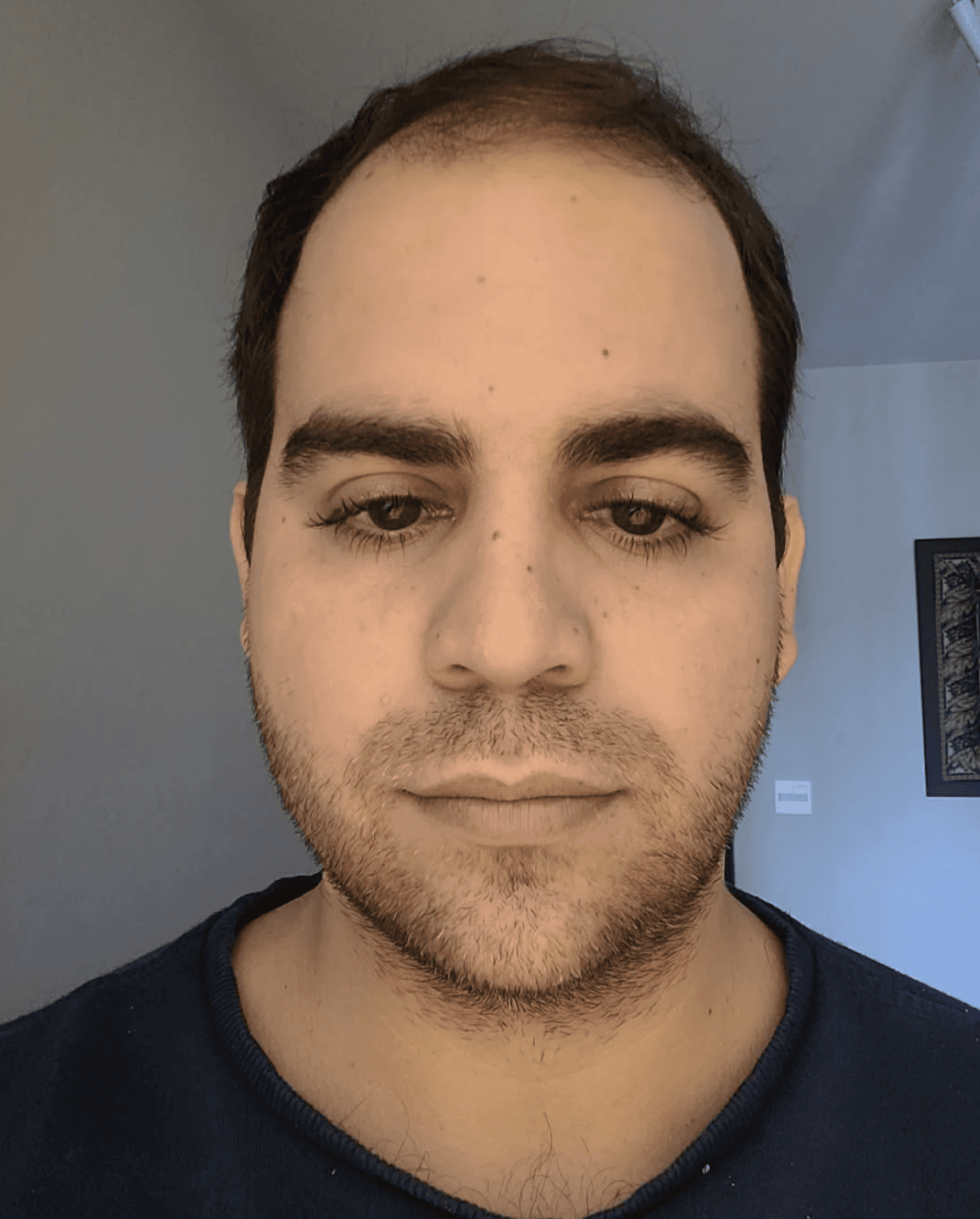 Blonde woman in a black long-sleeve and apron, arms crossed—minimalist studio portrait on a beige background.