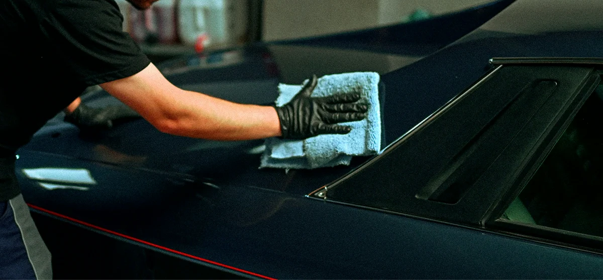 A gloved hand cleaning a car window with a microfiber cloth during glass detailing service