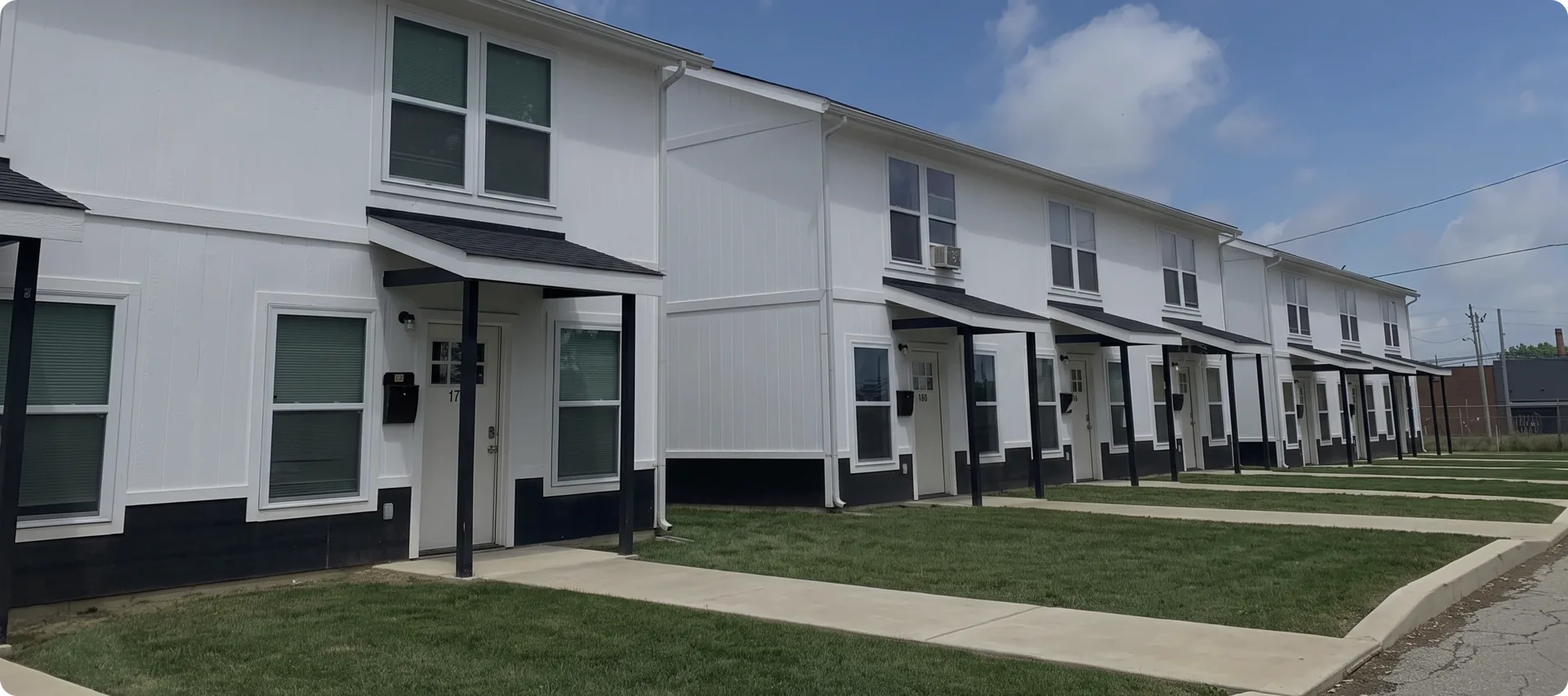 Suburban Triplex Builds: a row of white two-story townhome units with dark skirting and covered entries along a sidewalk