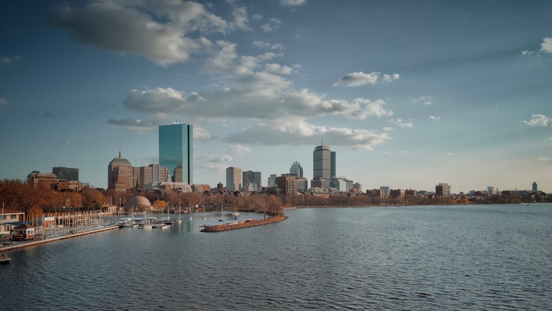Boston Back Bay skyline with the Charles River in the foreground under a partly cloudy sky.