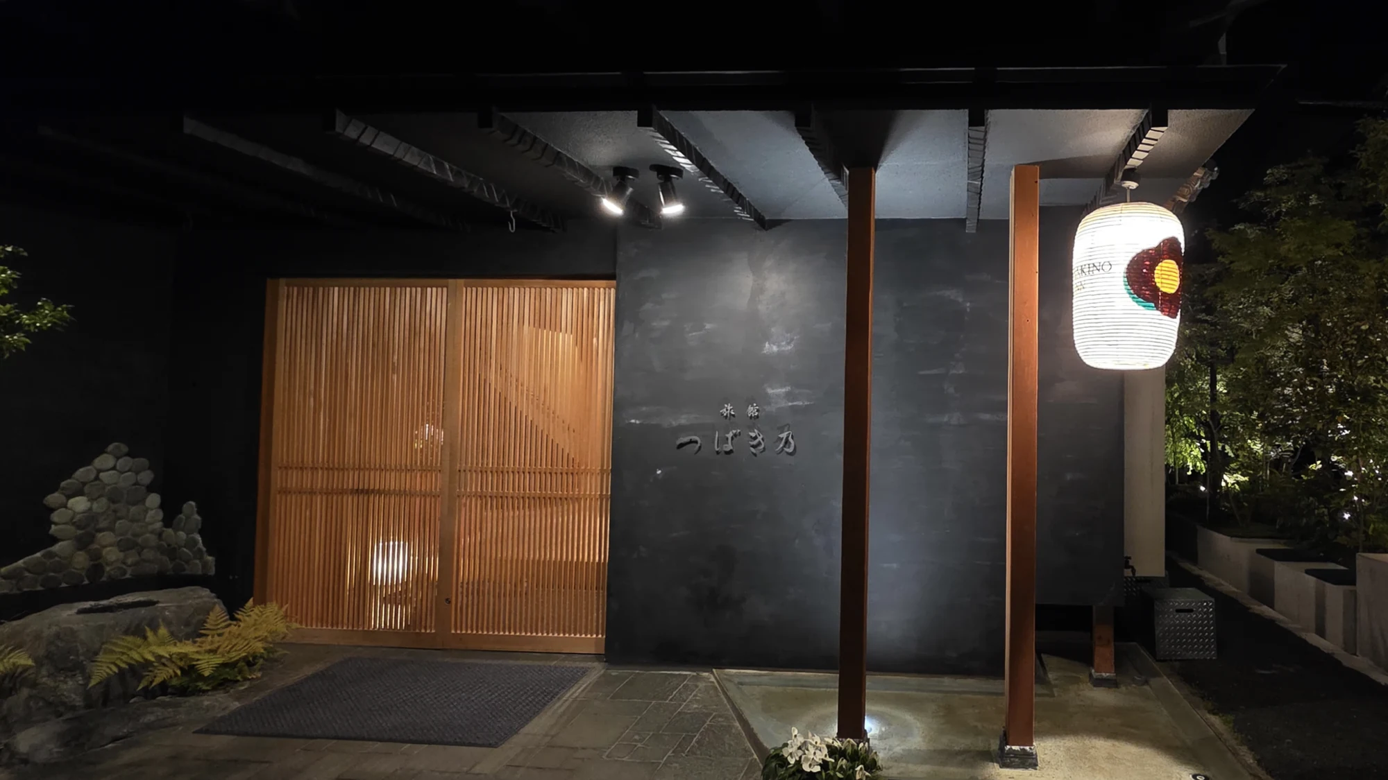 The lit timber-and-slate entrance of a contemporary Kinosaki inn at night.
