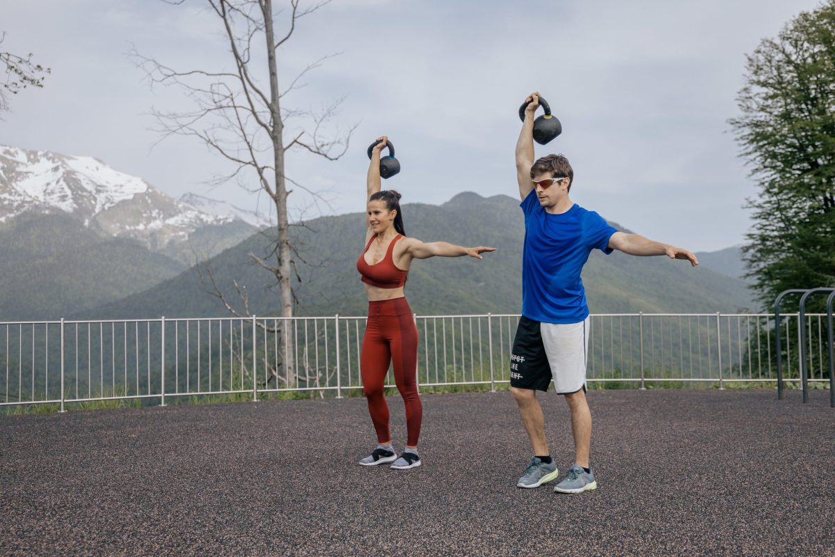 Two people exercise with kettlebells outdoors.