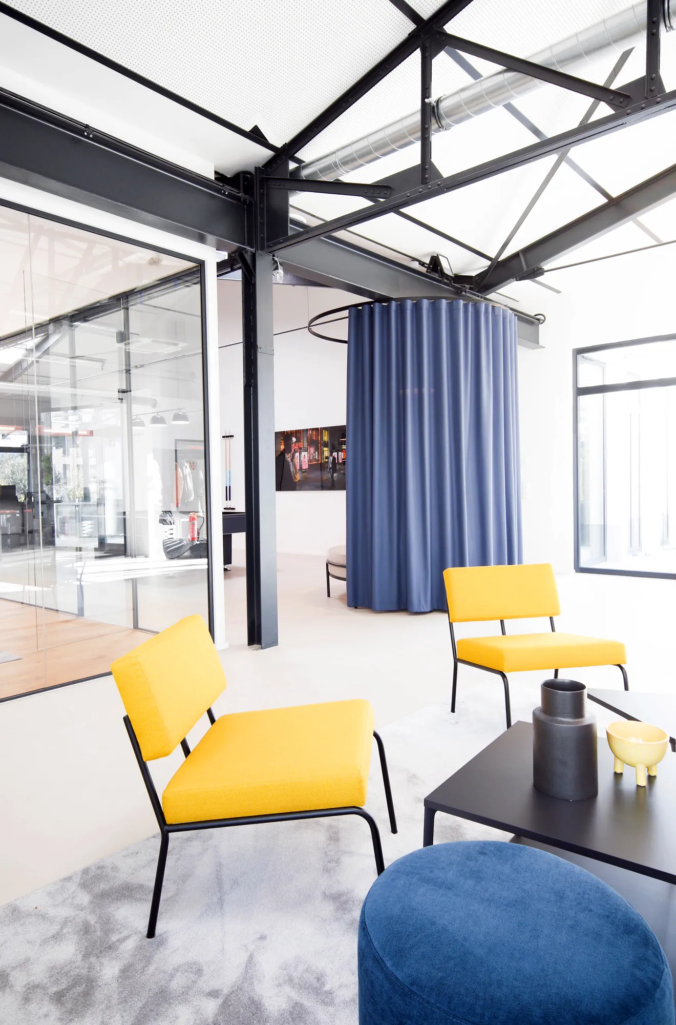 Yellow lounge chairs and blue pouf next to a blue curtain in the industrial loft.