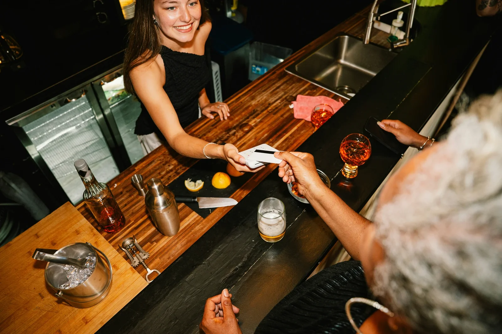 Bartender hands receipt to customer at bar counter during transaction, illustrating customer engagement and loyalty program enrollment.