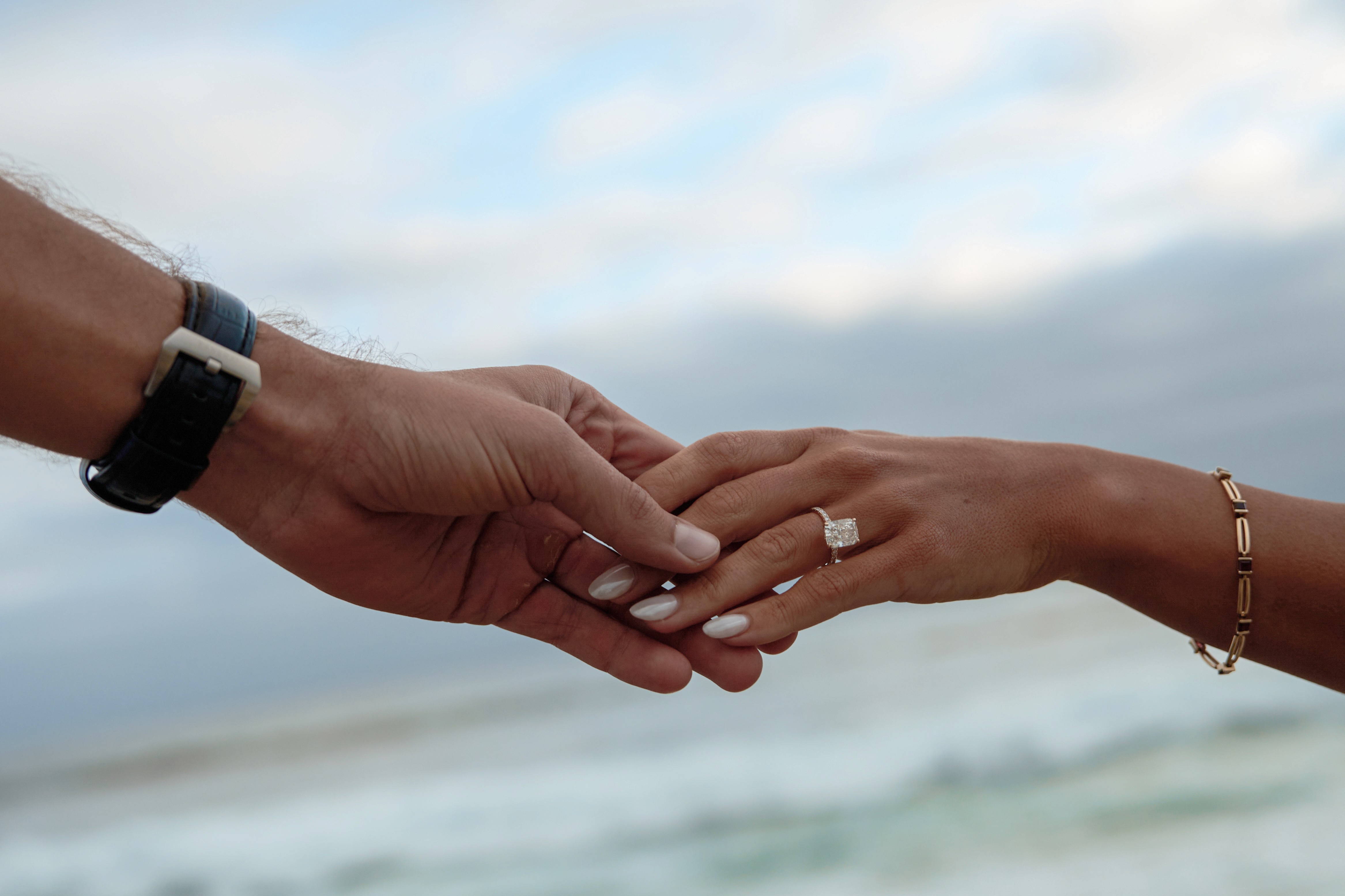 Two hands joined, with a cushion-cut diamond engagement ring