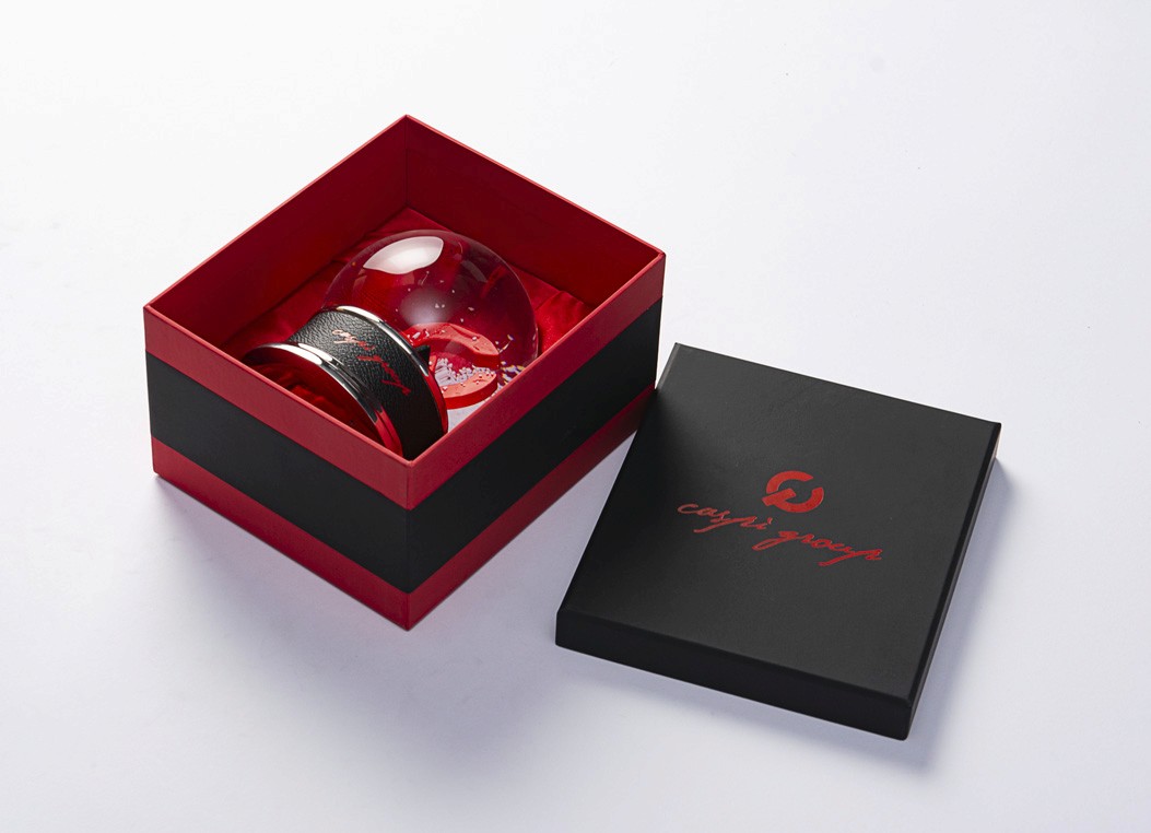 A snow globe nestled securely inside a gift box lined with red satin fabric.