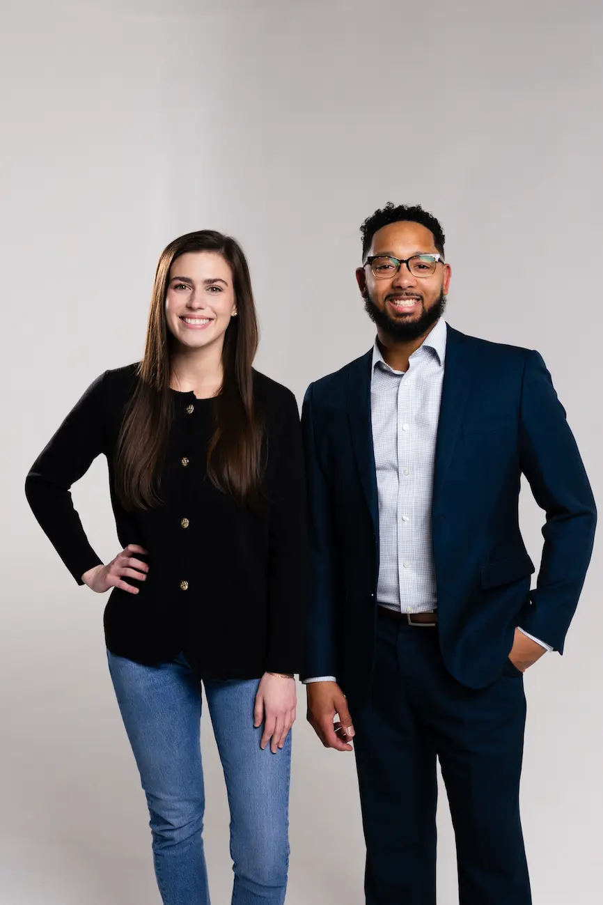 Chris Lewis and Kaylee sit together in a modern office space, smiling during a relaxed conversation. The setting features a warm wooden backdrop and natural light, reflecting the friendly and professional atmosphere of Chris Lewis Home Loans.