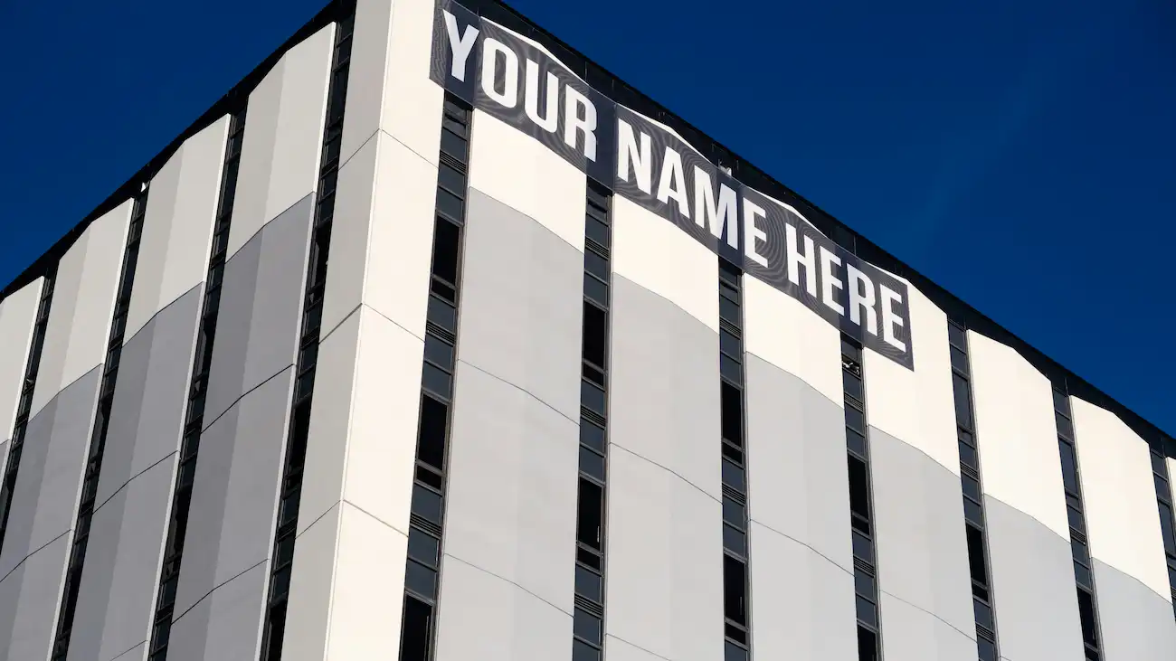 Large building facade with a banner reading “YOUR NAME HERE” — representing title sponsorship and naming rights, where a sponsor name becomes part of an event or tournament title.