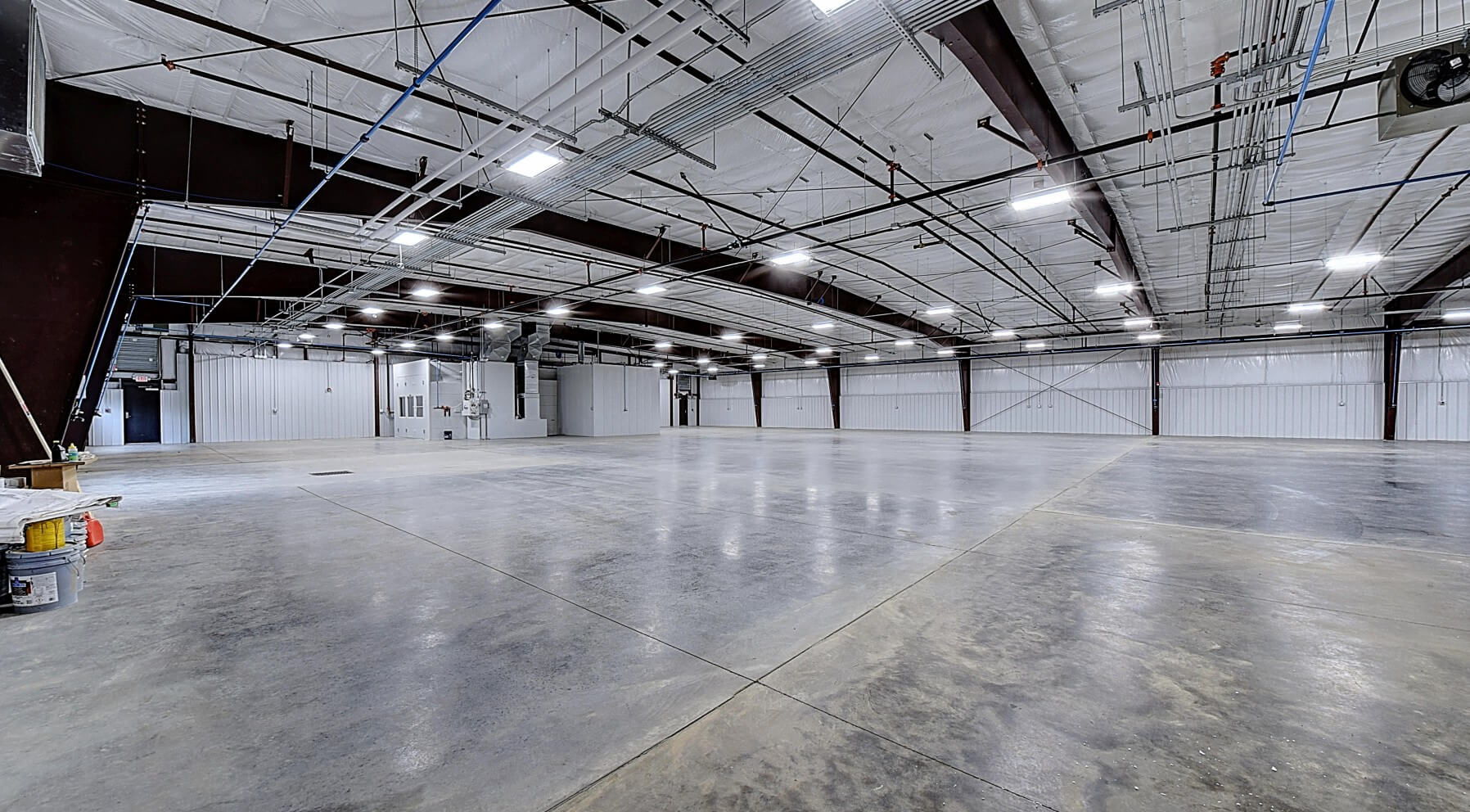 A spacious, empty industrial warehouse with polished concrete floors and high ceilings supported by metal beams.