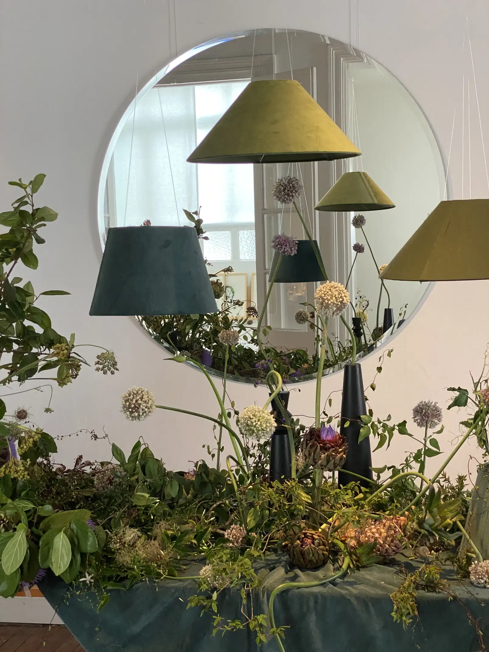 Instalación botánica con flores esféricas y lámparas suspendidas frente a espejo para composición artística contemporánea.