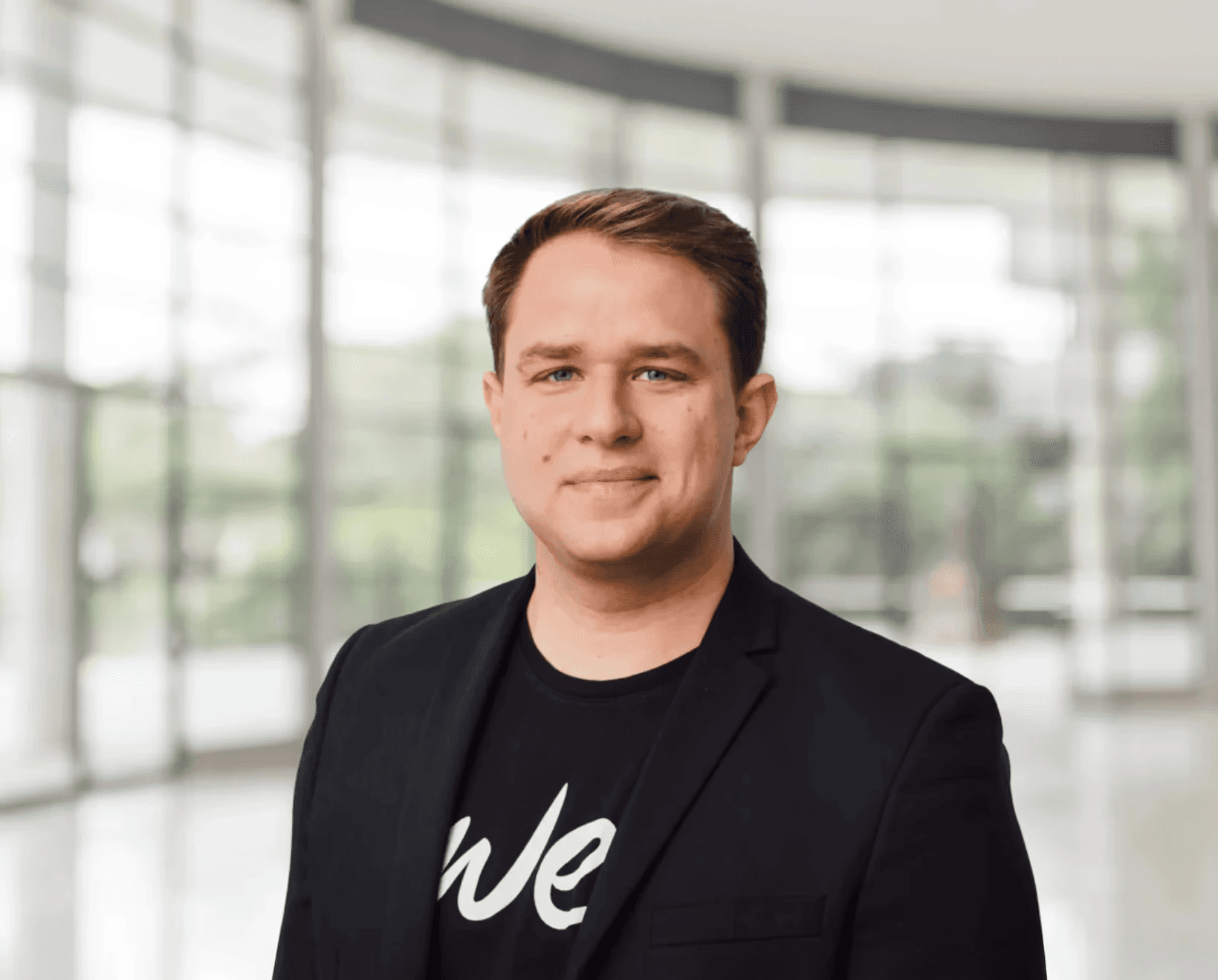 Junger Geschäftsmann im schwarzen Sakko steht in modernem Bürogebäude