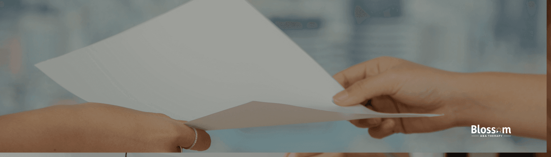 Two ABA therapist hands exchange a paper across a desk in a high-rise office with city view in background