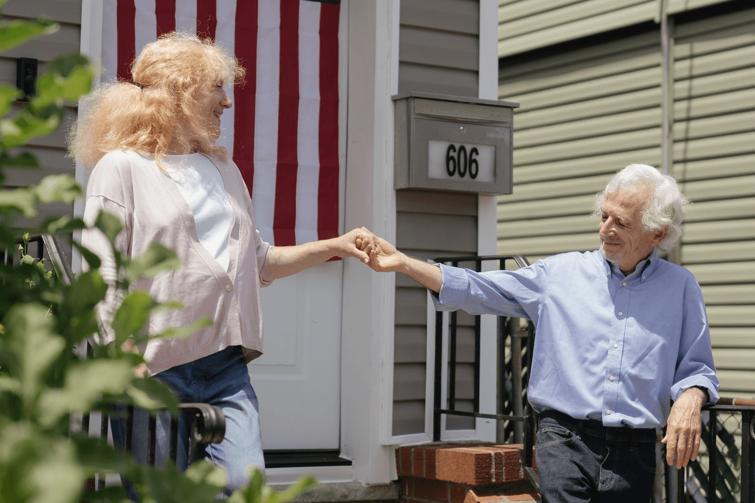 Two neighbors greet each other with a fist bump on a front porch.