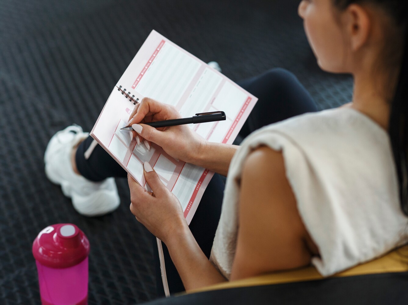 woman writing out her plan for the best gym cardio for weight loss alongside strength training exercises in a notebook