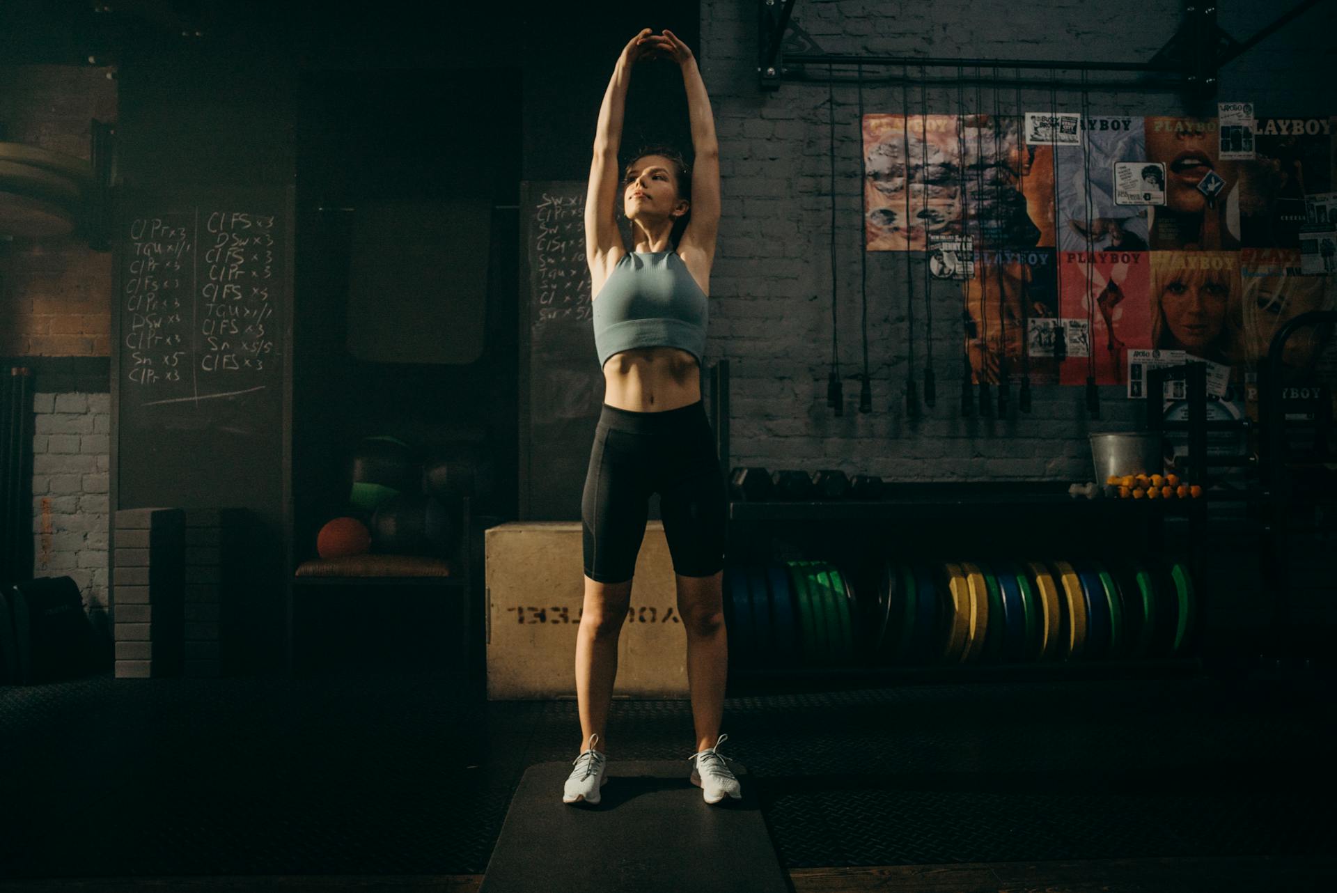 Woman stretching with arms overhead in a gym.